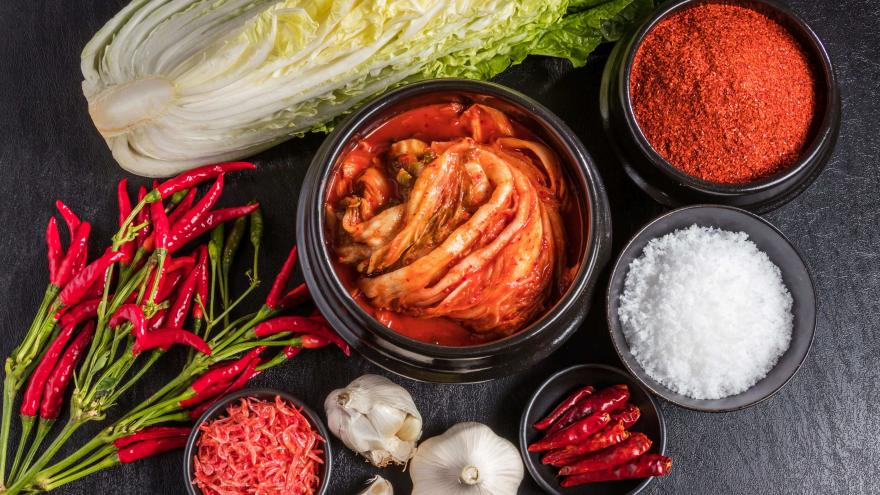 Auf einem Tisch liegen Kimchi, Chilis, Kohl und weitere Zutaten wie Knoblauch.